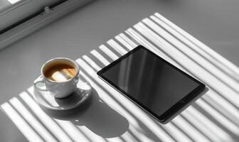 Tablet on a light gray table with a cup of tea on the left, sunlight from window photo