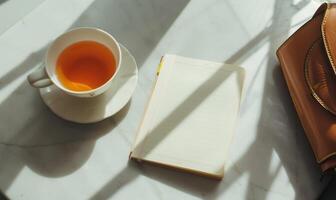 Closed notebook on a light gray table with a cup of tea on the left and a handbag on the right photo