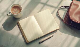 Closed notebook on a light gray table with a cup of tea and a handbag photo