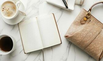 Closed notebook on a light gray table with a cup of coffee on the left and a handbag on the right photo