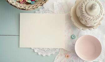 White blank card on a pastel ivory table, with a crochet doily and a small bowl of colorful buttons photo