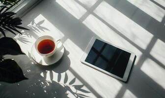 Tablet on a light gray table with a cup of tea on the left, sunlight from window photo