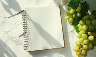Closed notebook on a white table with a bunch of grapes photo