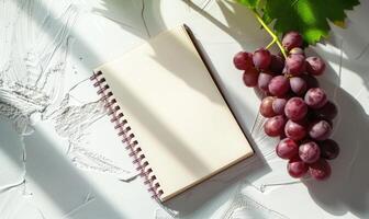 Closed notebook on a white table with a bunch of grapes photo