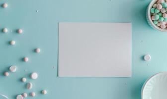 White blank card on a pastel sky blue table, with a white ceramic bowl and pastel colored beads photo
