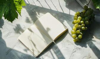 Closed notebook on a light gray table with a bunch of grapes photo
