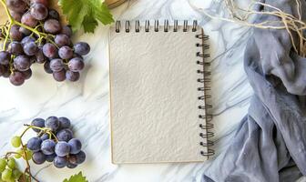 Closed notebook on a white table with a bunch of grapes photo