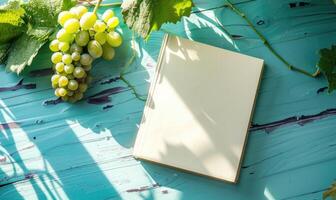 Closed notebook on a light blue table with a bunch of grapes on the left photo