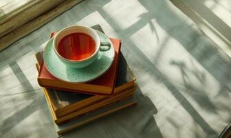 Stack of books with a cup of tea on a light gray table, soft shadows from window photo