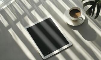 Tablet on a light blue table with a cup of tea on the right, shadow from window, top view photo