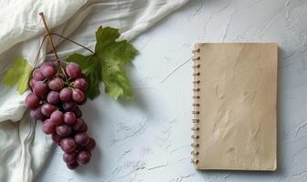 Closed notebook on a white table with a bunch of grapes photo