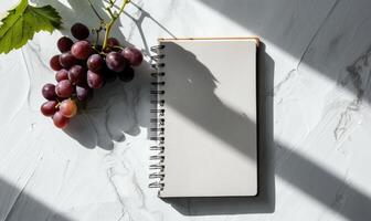 Closed notebook on a white table with a bunch of grapes photo