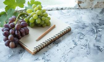 Closed notebook on a light gray table with a bunch of grapes photo