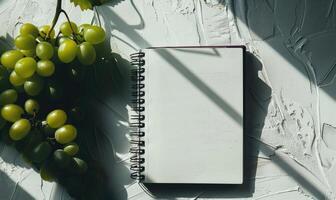 Closed notebook on a white table with a bunch of grapes photo