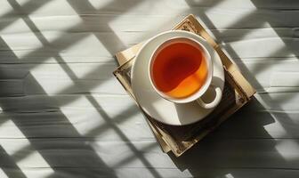 Stack of books with a cup of tea on a light gray table, soft shadows from window photo