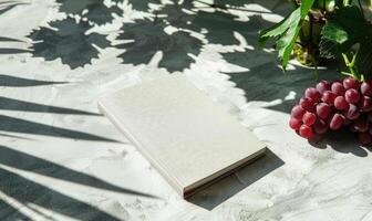 Closed notebook on a light gray table with a bunch of grapes on the right photo
