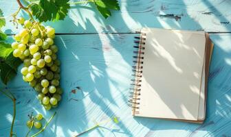 Closed notebook on a light blue table with a bunch of grapes on the left photo