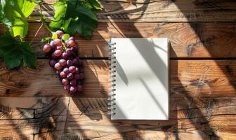 Notebook on a wooden table with a bunch of grapes photo