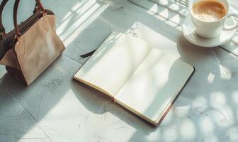 Closed notebook on a light gray table with a cup of coffee on the right and a handbag on the left photo