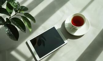 Tablet on a light blue table with a cup of tea on the right, shadow from window, top view photo
