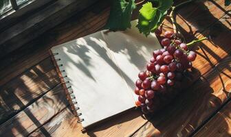 Notebook on a wooden table with a bunch of grapes photo