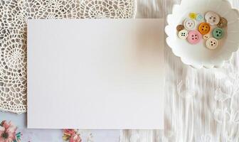 White blank card on a pastel ivory table, with a crochet doily and a small bowl of colorful buttons photo
