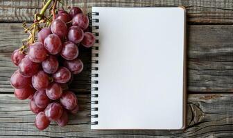 Notebook on a wooden table with a bunch of grapes photo