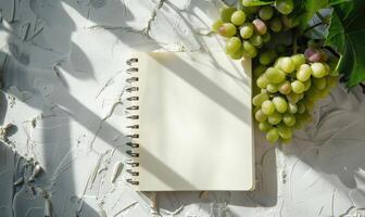 Closed notebook on a light gray table with a bunch of grapes photo