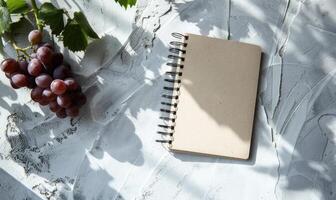 Closed notebook on a light gray table with a bunch of grapes photo