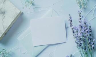 White blank card on a pastel periwinkle table, with a sprig of lavender and a small notebook photo