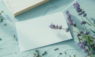 White blank card on a pastel periwinkle table, with a sprig of lavender and a small notebook photo