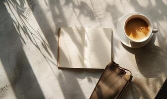 Closed notebook on a light gray table with a cup of tea on the right and a handbag on the left photo