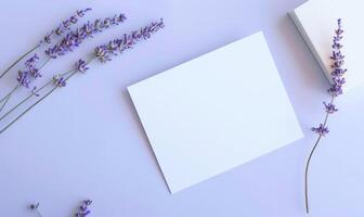 White blank card on a pastel periwinkle table, with a sprig of lavender and a small notebook photo