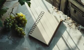Closed notebook on a light gray table with a bunch of grapes photo