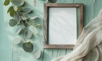 White blank card in a rustic wooden frame on a pastel mint green table, with a sprig of eucalyptus and a linen cloth photo