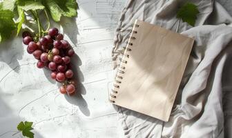 Closed notebook on a light gray table with a bunch of grapes photo