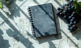 Closed notebook on a light gray table with a bunch of grapes photo