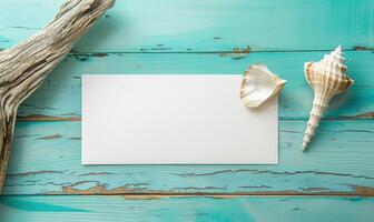 White blank card on a pastel turquoise background, with a seashell and a piece of driftwood photo