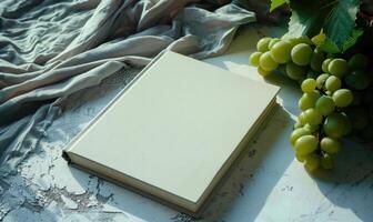 Closed notebook on a light gray table with a bunch of grapes on the right, soft window light photo