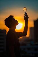 a man holding up a light bulb at sunset photo
