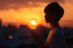 a young man holding a light bulb in front of a sunset photo