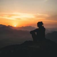 a person sitting on top of a mountain at sunset photo