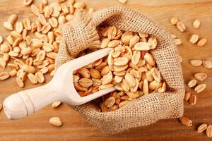 Roasted peeled peanuts in rustic bag on wooden table photo