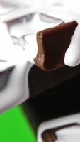 Close-up of chocolate with white cream. Stock clip. White liquid cream flows down chocolate bar. Sweet chocolate with cream on green background video