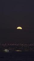 Night background of a big city and river. Action. Beautiful full moon hiding behind the clouds in the dark sky. video