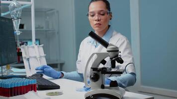 Chemistry scientist using research equipment in laboratory on desk with petri dish, micropipette, vacutainers and microscope. Scientific woman typing on computer for development video