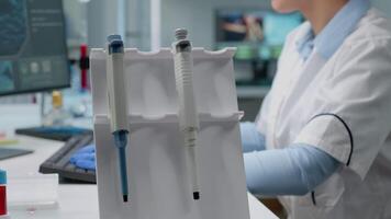 Close up of scientific micropipette on laboratory desk used by biotechnology specialist in lab coat while typing on computer. Woman working in medical development and innovation industry video