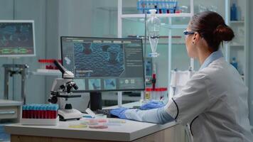 Innovation scientist studying petri dish with liquid bacteria while using modern computer with cell animation in laboratory. Woman with lab coat and glasses doing pharmaceutical research video