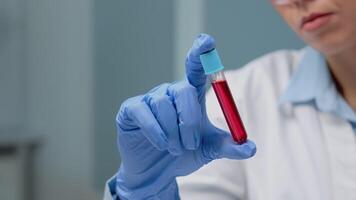 Close up of vacutainer filled with blood for investigation in laboratory. Scientist with gloves looking at transparent glassware tool with liquid solution used by doctor for science video