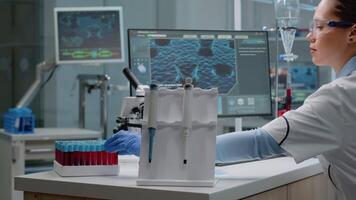 Scientist woman sitting in laboratory with chemical technology on desk. Biochemistry doctor with pipette, blood vacutainers, microscope, typing on computer for microbiology experiment video